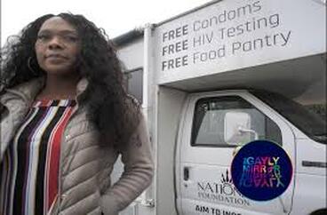 A picture of Tykira Spurill. She has curly brown hair, dark skin, and a fashionable outfit. She stands by a white truck advertising free condoms, HIV testing, and food pantry.